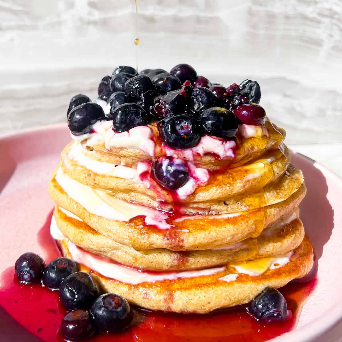 Protein pancakes without protein powder with blueberries on top on a pink plate.
