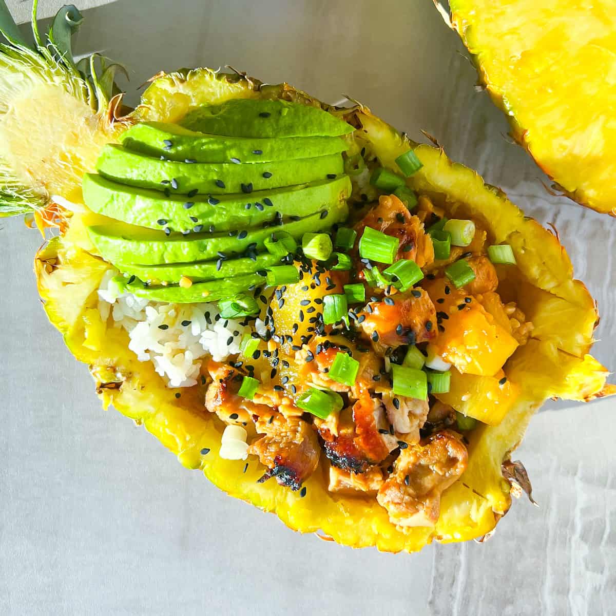 Teriyaki chicken pineapple bowls filled with chicken, rice, and garnished with avocado, green onions.