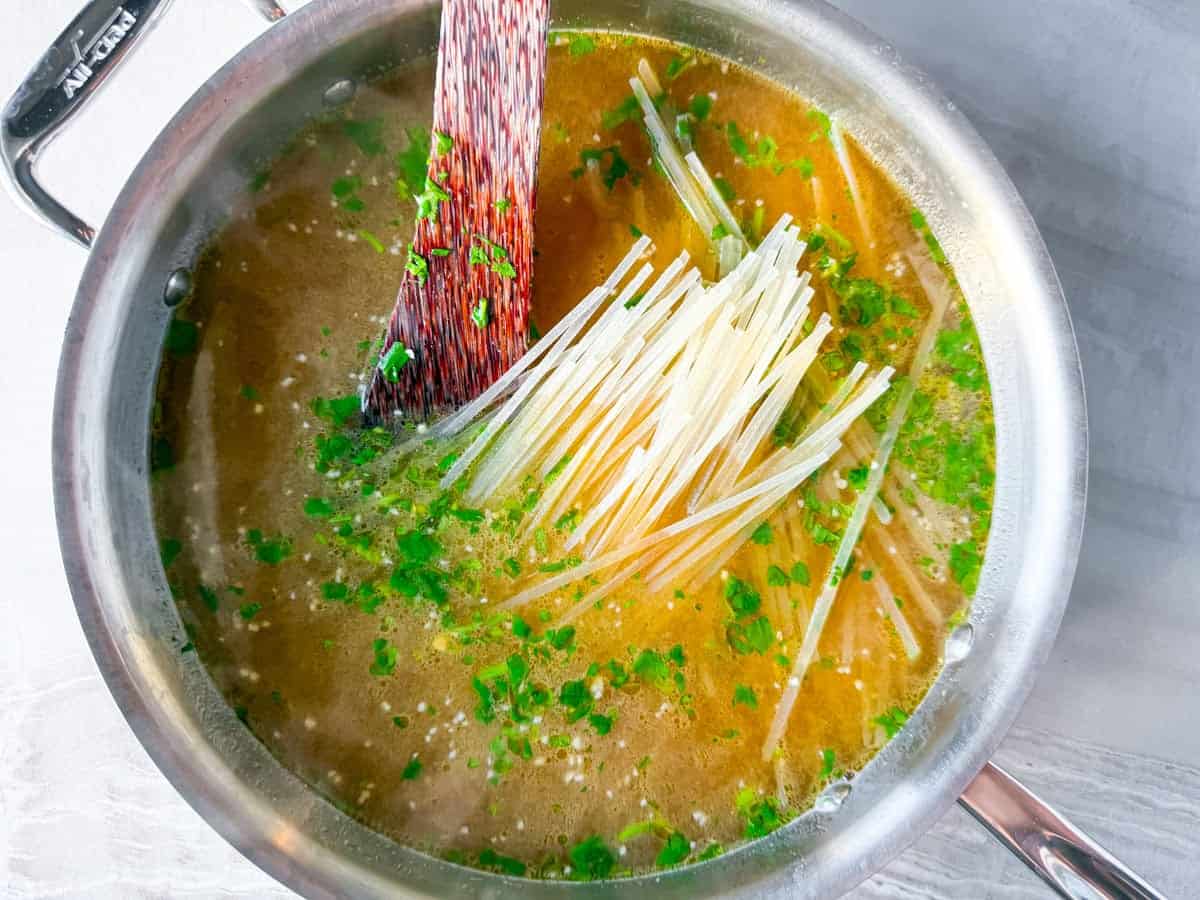 Rice noodles uncooked sitting inn the chicken broth in the pot.