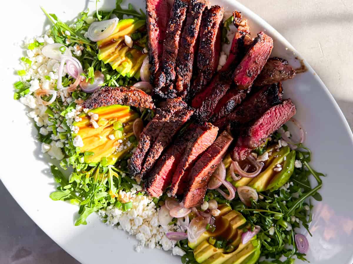 Assembled steak salad with arugula, avocado, feta, on a large platter.