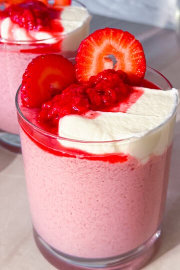 Finished raspberry chia pudding in a cup topped with raspberries and greek yogurt.