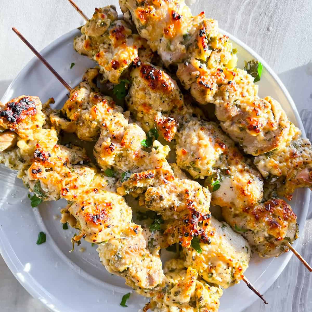 Four garlic parmesan chicken skewers on a white plate.