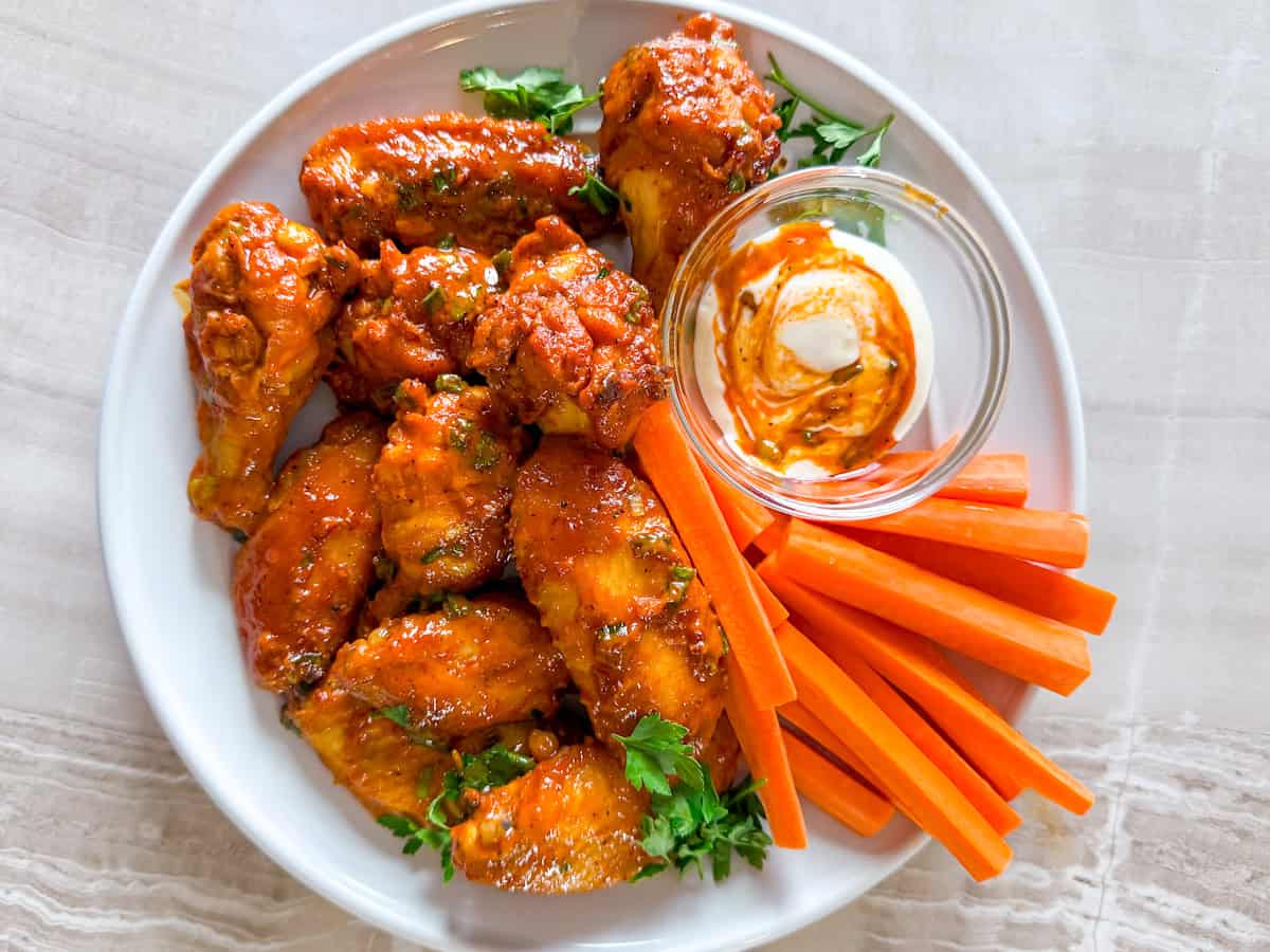 Gluten-free chicken wings on a white plate with sauce on the side.