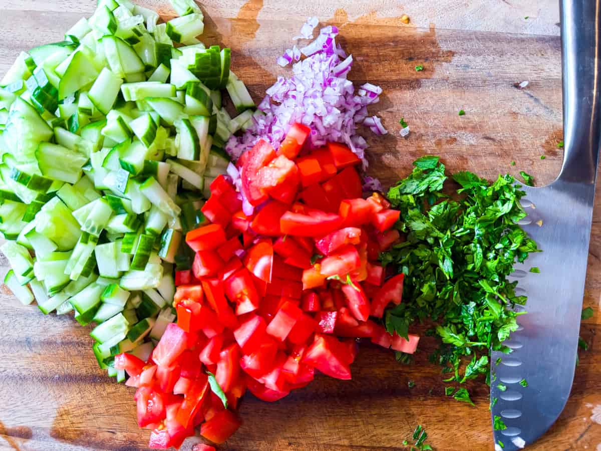 Mediterranean salad vegetables chopped on a wooden cutting board.