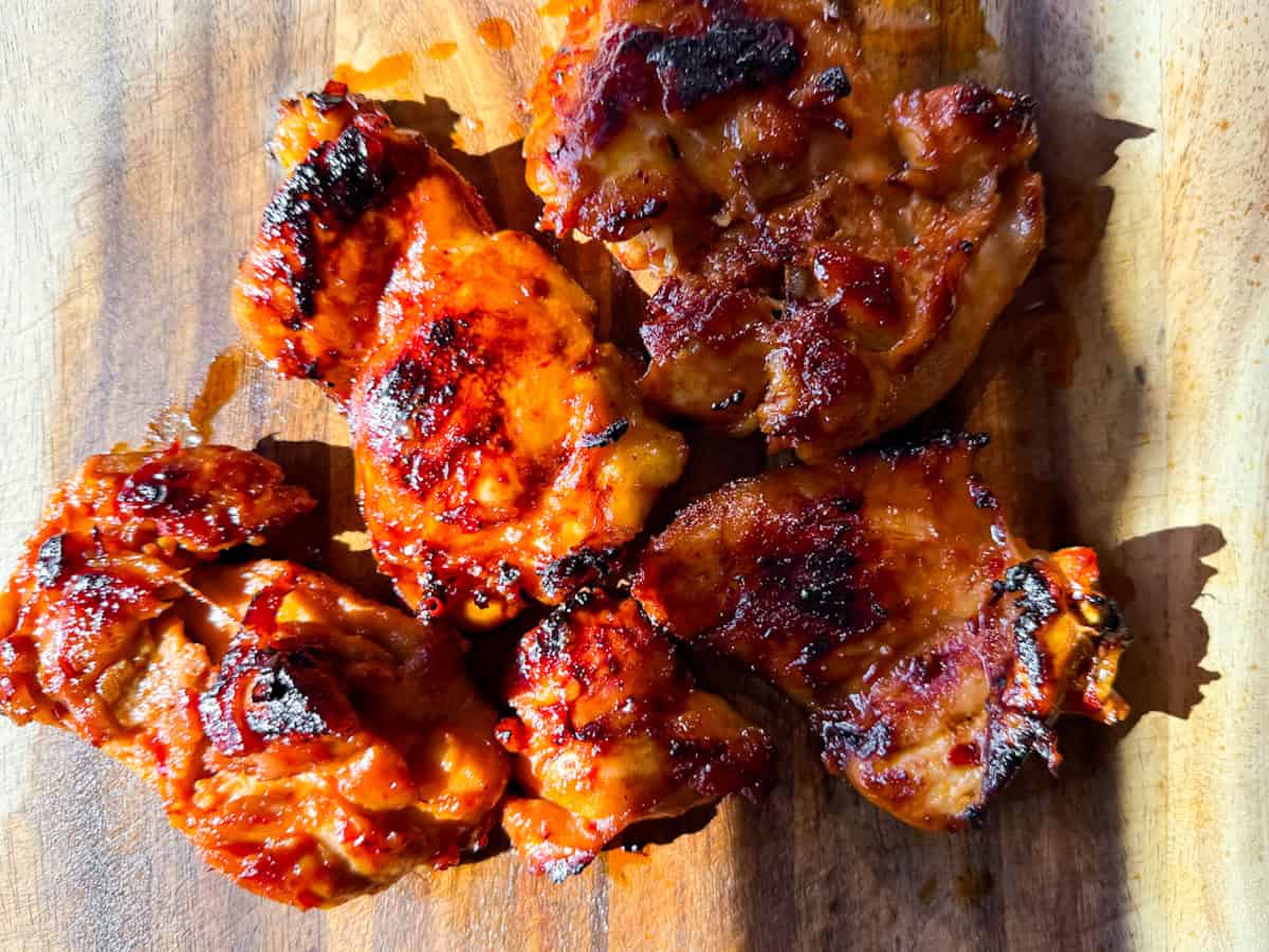 Harissa honey chicken thighs grilled and sitting on a wooden cutting board.