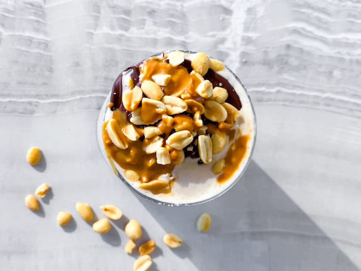 Peanut butter smoothie without banana in a glass topped with peanuts and chocolate.