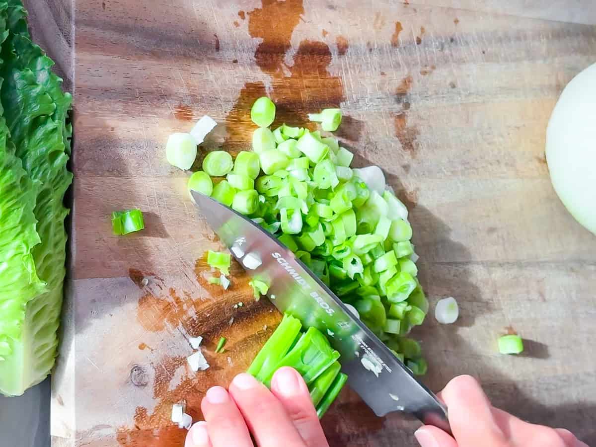 Green onions being chopped on a wooden cutting board.