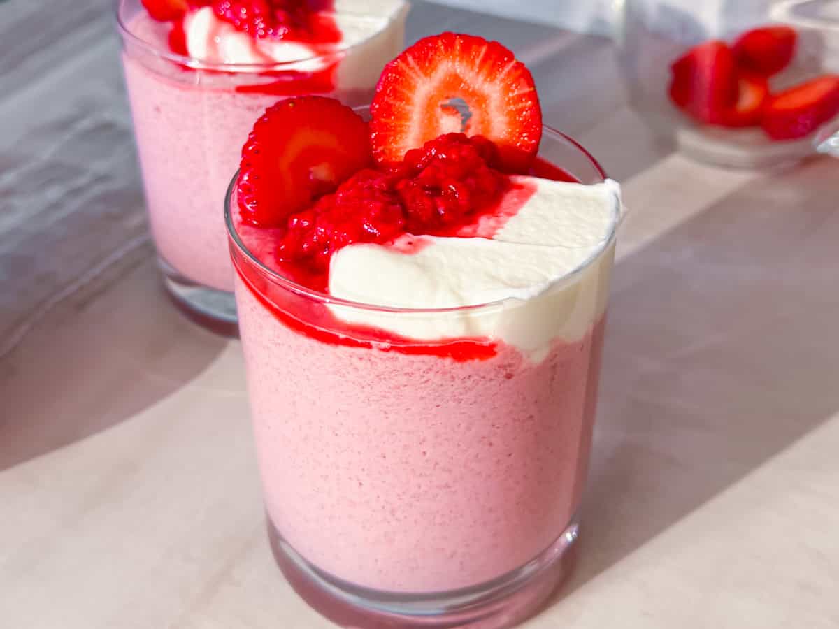 Raspberry chia seed pudding in a clear cup topped with fresh raspberries and greek yogurt.
