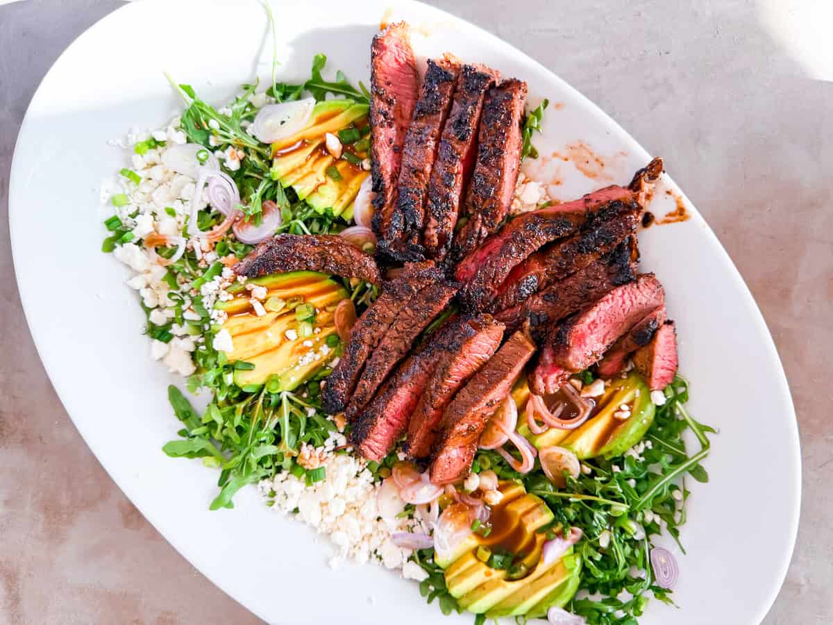 Finished steak arugula salad on a large white platter.