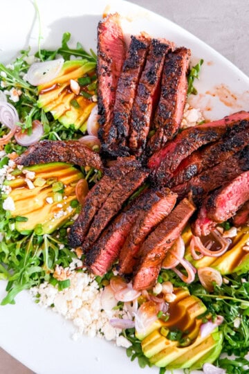 Finished steak and arugula salad on a large white plate.