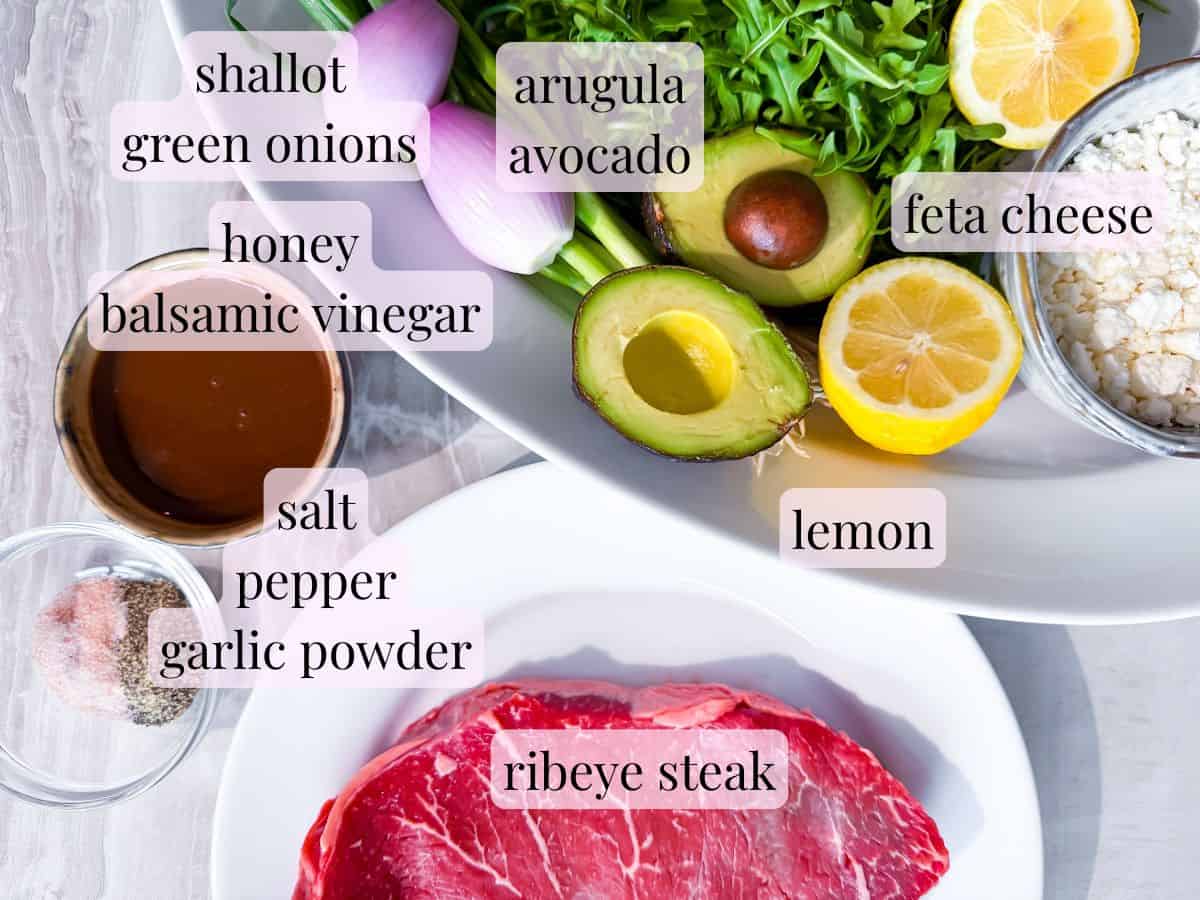 Ingredients like ribeye, arugula, avocado, and balsamic dressing for a steak and arugula salad.