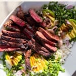 Steak arugula salad on a white platter.