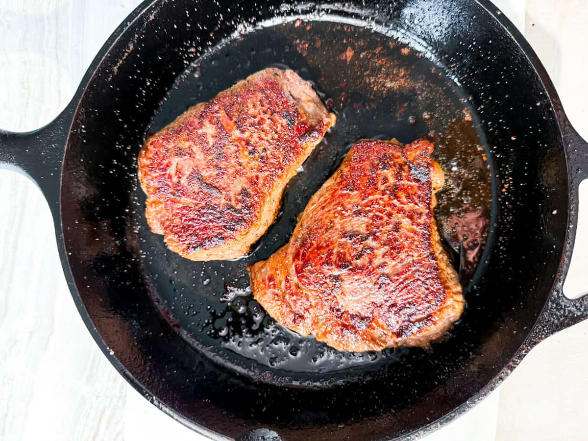 two steaks searing in a cast iron.