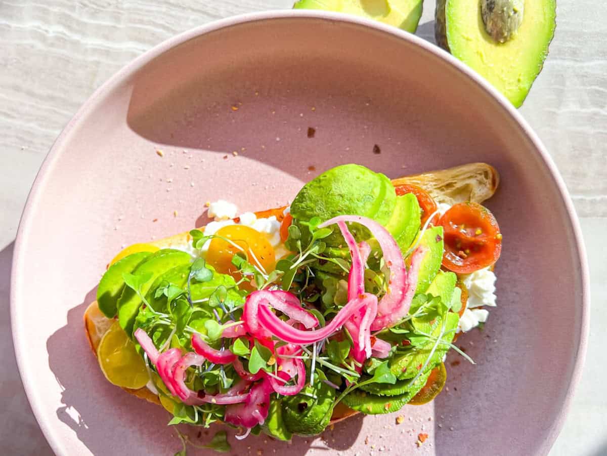 Cottage cheese avocado toast topped with pickled onions and microgreens.