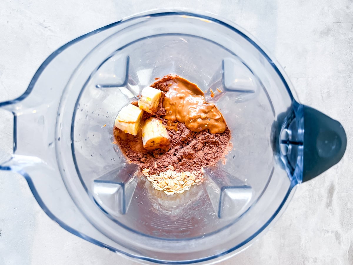 Cocoa powder, banana, peanut butter, oats, almond milk, and maple syrup in a blender.