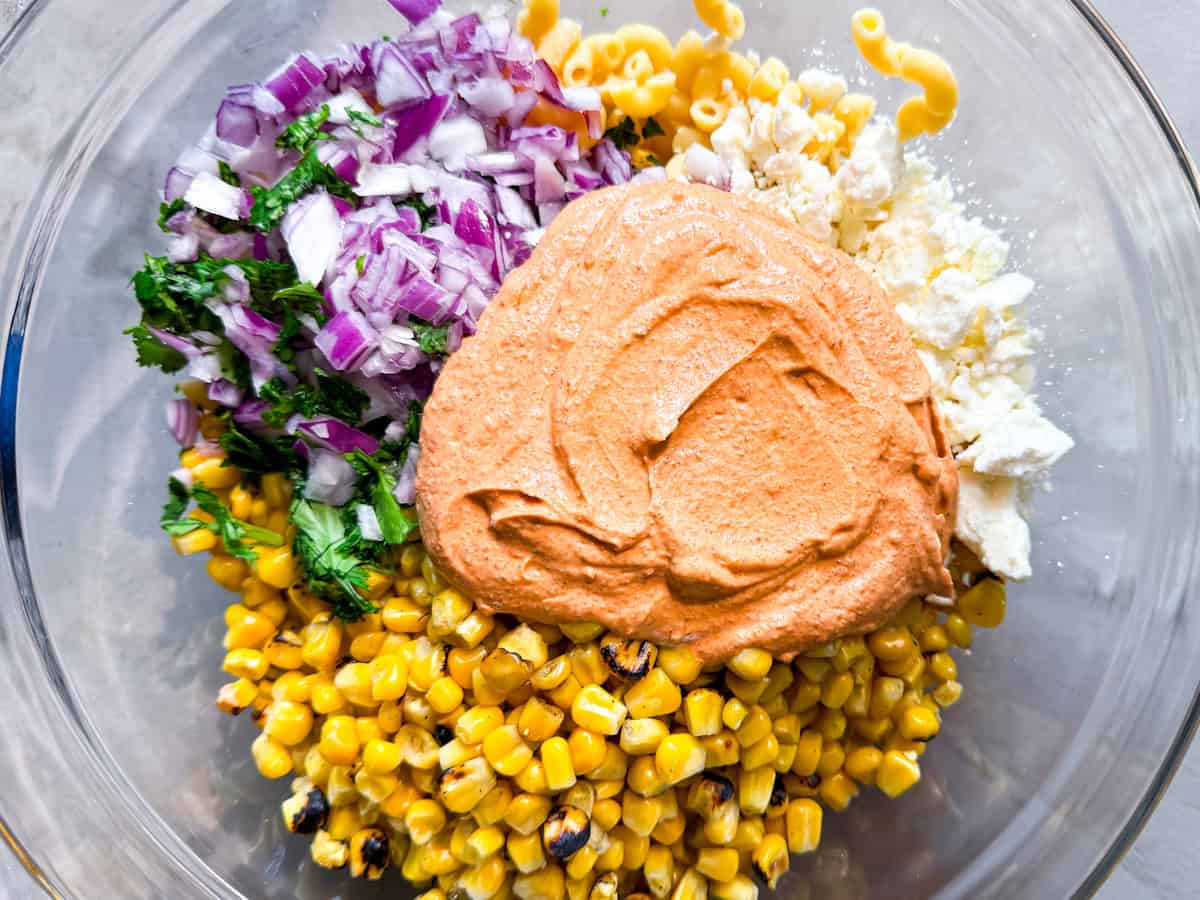 Elote pasta salad ingredients combined in a bowl.