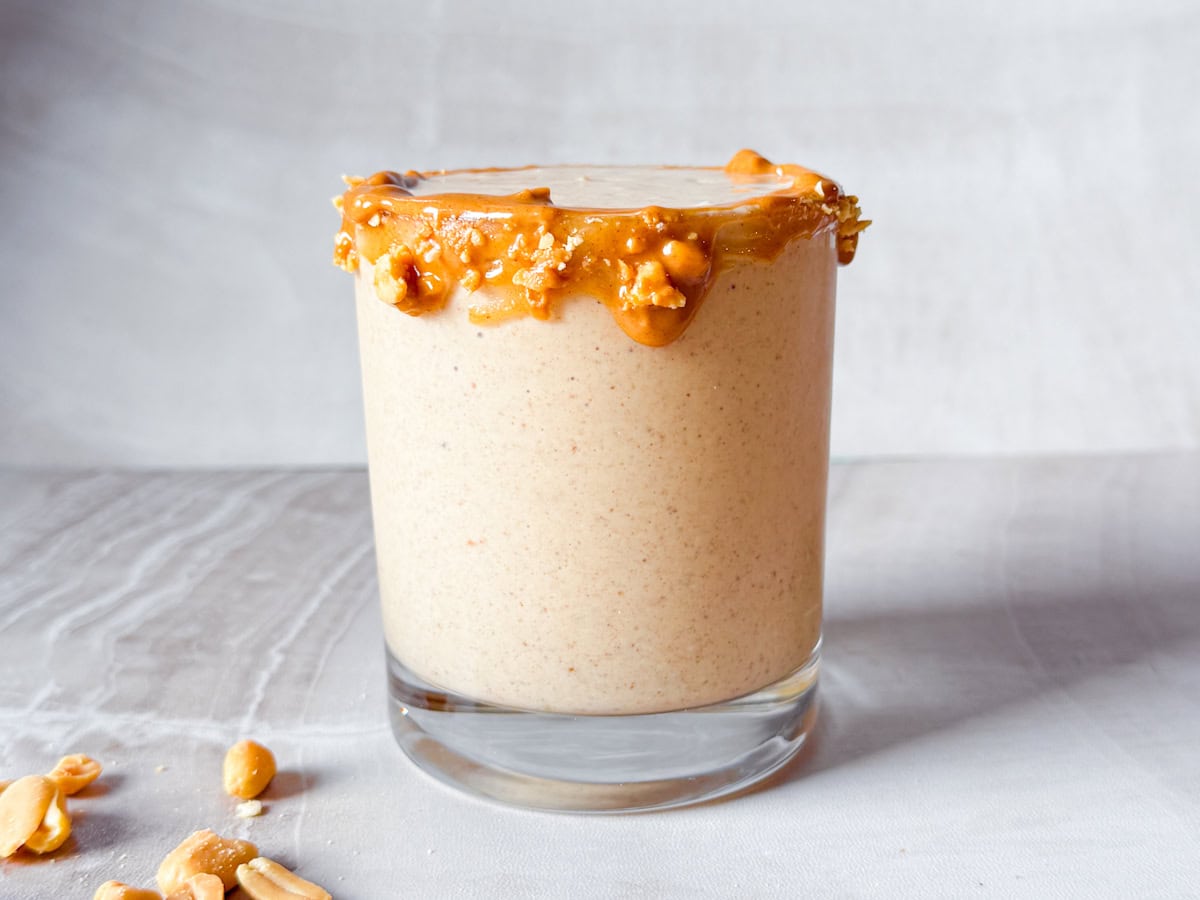Peanut butter smoothie in a glass topped with peanuts.