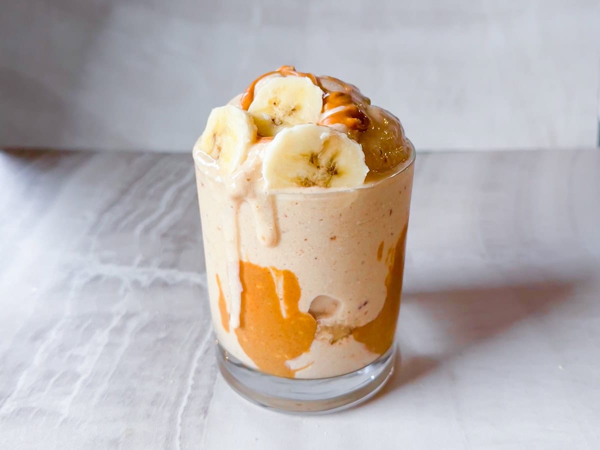 Finished peanut butter and banana smoothie in a cup topped with sliced bananas and peanut butter.
