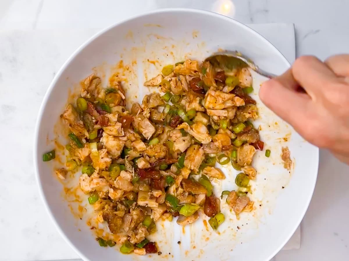 Chicken, bacon, spices, and hot sauce mixed in a bowl.