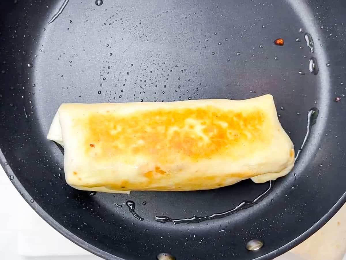 Buffalo chicken wrap being seared in a skillet.
